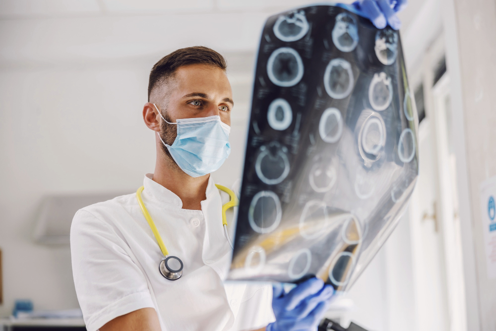 attractive-dedicated-young-doctor-standing-in-hospital-with-face-mask-and-rubber-gloves-and-looking-at-x-ray-of-patient-s-brain.jpg